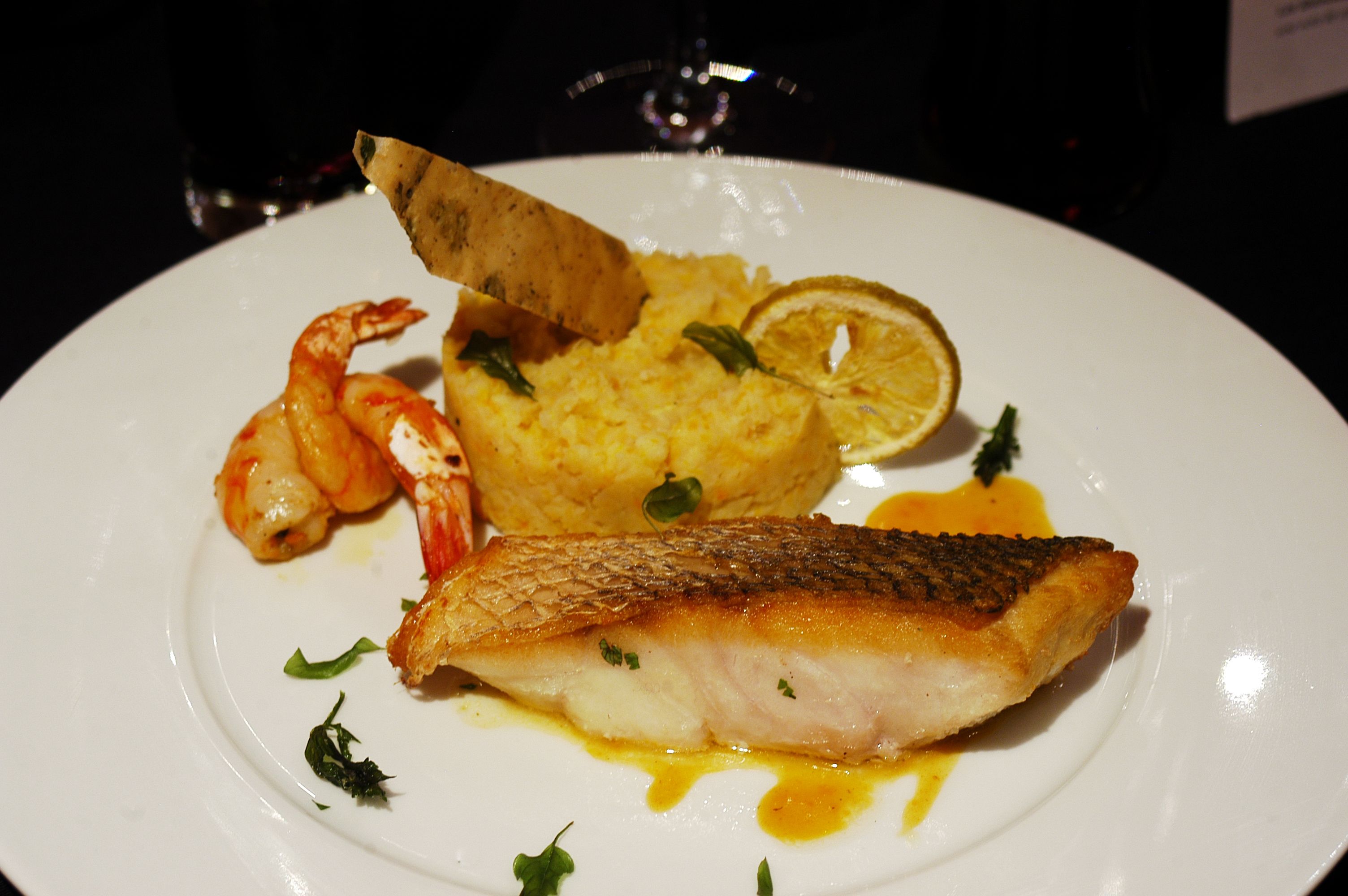 Un plato con un trozo de pescado, camarones y puré de papas.