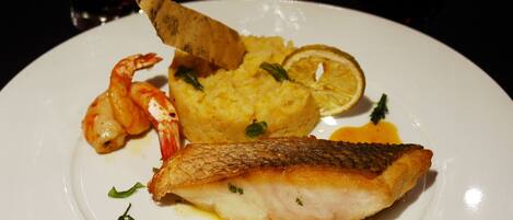 Un plato con un trozo de pescado, camarones y puré de papas.
