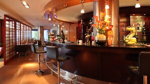 Un espace bar avec des tabourets, un comptoir incurvé et des éléments décoratifs tels que des fleurs et un masque.
