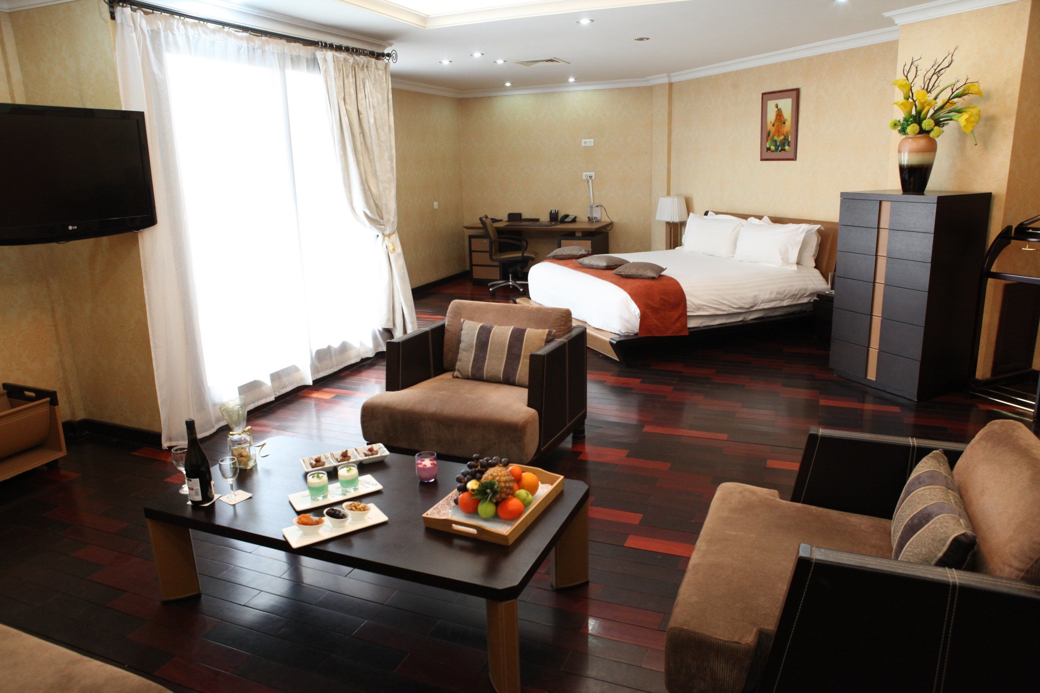 Habitación de hotel con cama, escritorio, televisión y zona de estar con una bandeja de fruta.