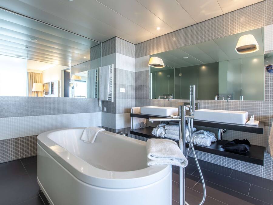 Un baño moderno con una bañera independiente, un espejo grande y un tocador con lavamanos y perchero para toallas.