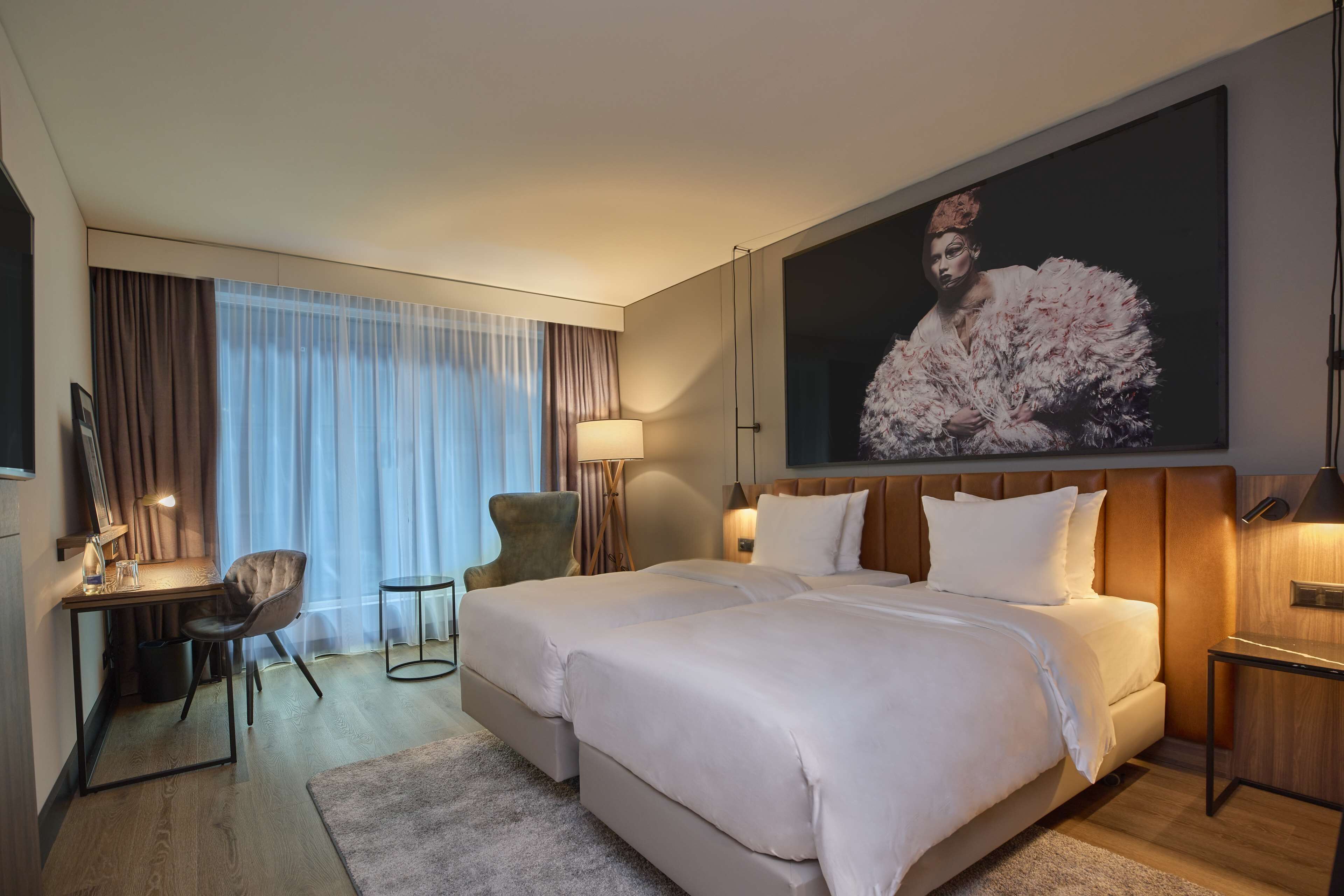 A hotel room with a large bed, a desk with a chair, a TV, and a painting on the wall.