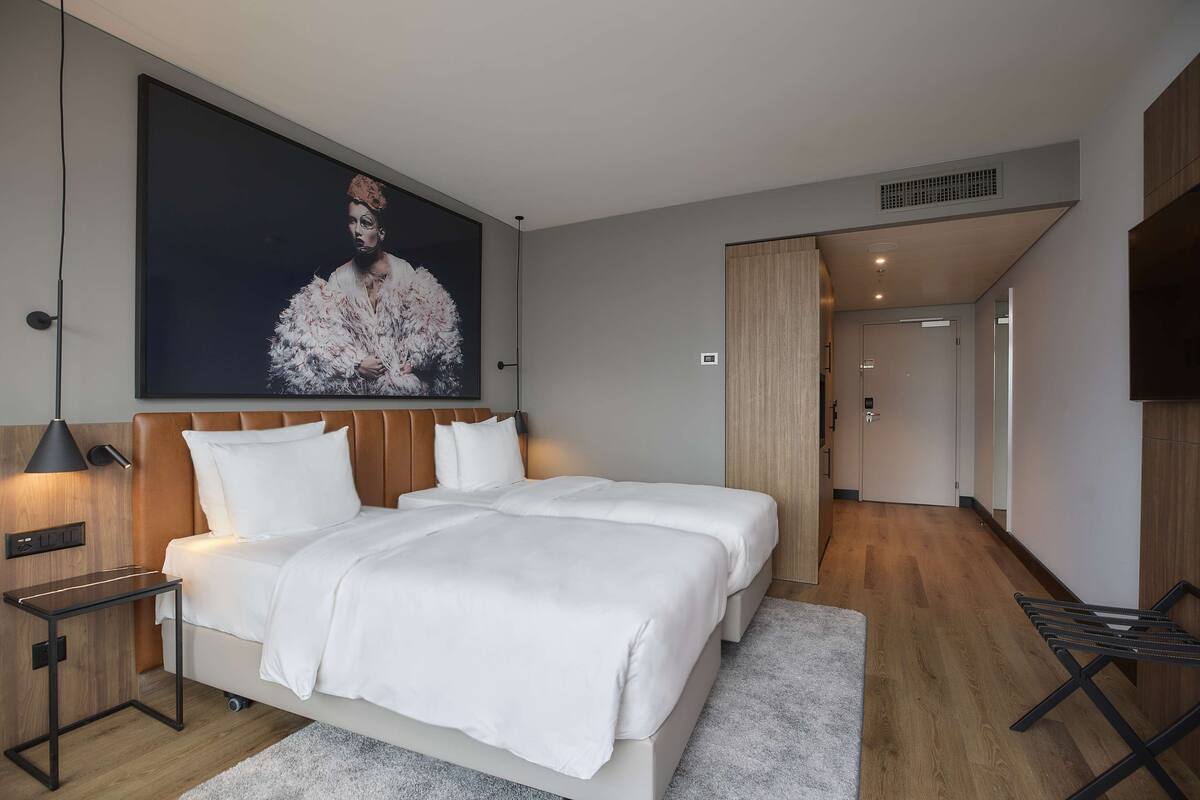 Una habitación de hotel moderna con una cama grande, una mesita de noche, un televisor montado en la pared y una puerta que da a otra habitación.