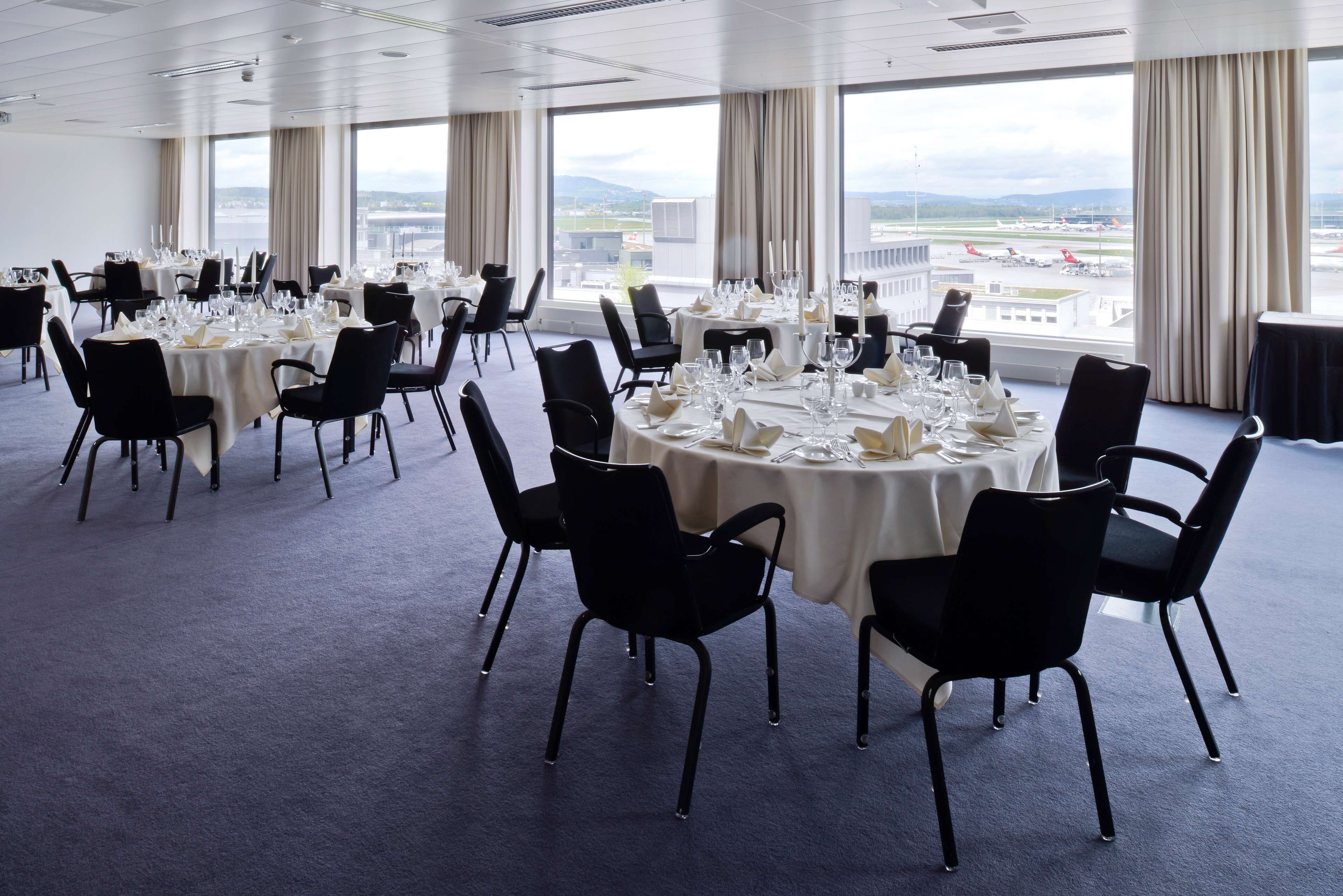 A conference room with round tables, black chairs, and a view of an airport.