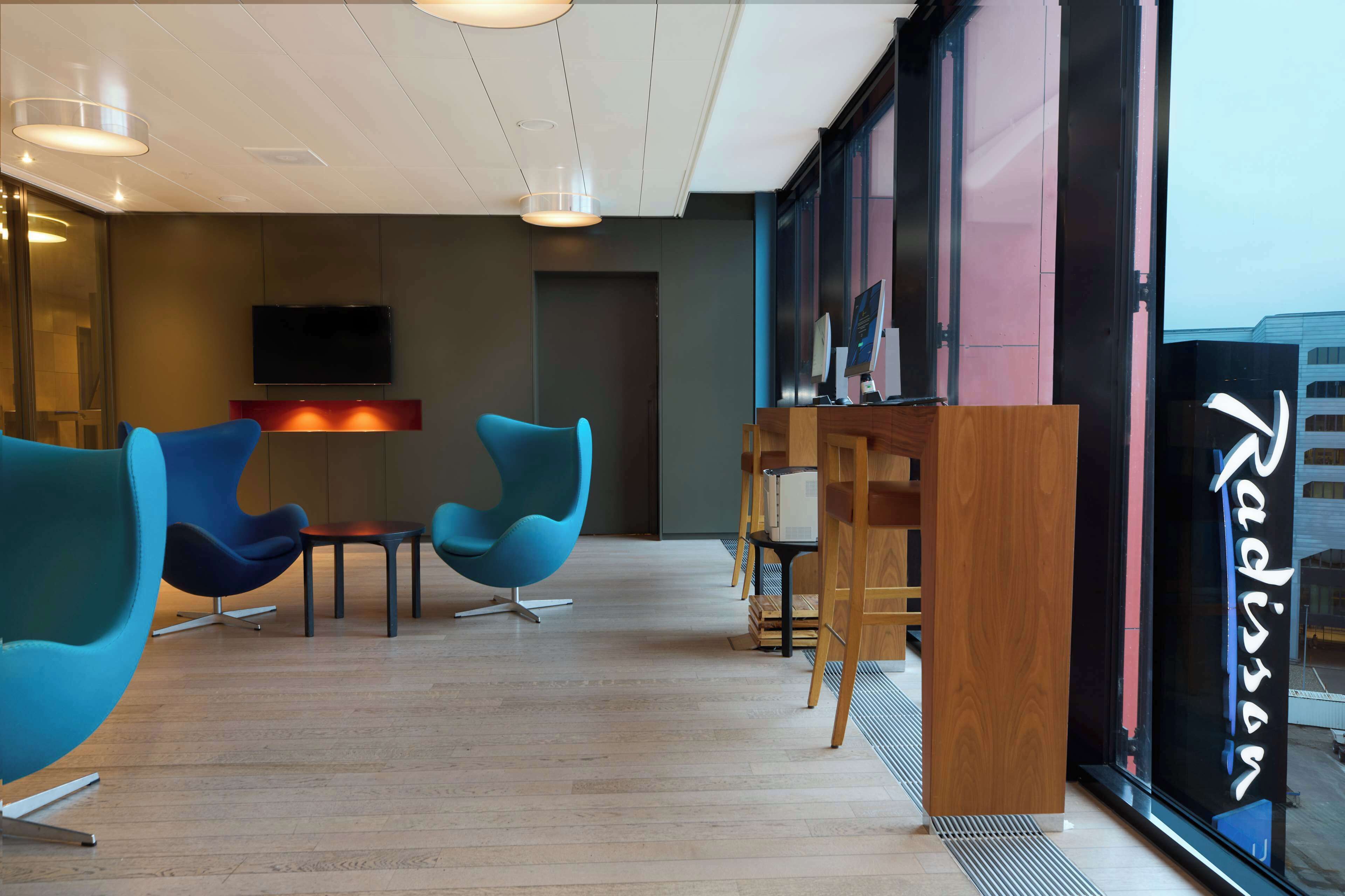 Interior moderno com cadeiras azuis, um balcão de recepção de madeira e uma janela grande com o nome 'Radisson'.