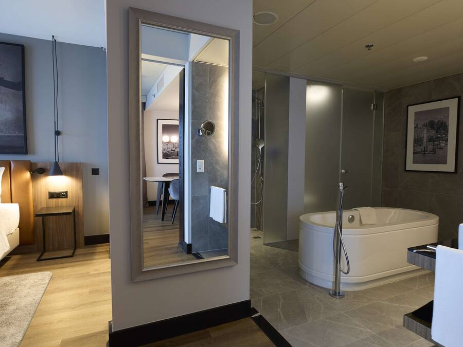 A modern hotel bathroom with a large mirror, a bathtub, and a shower area.
