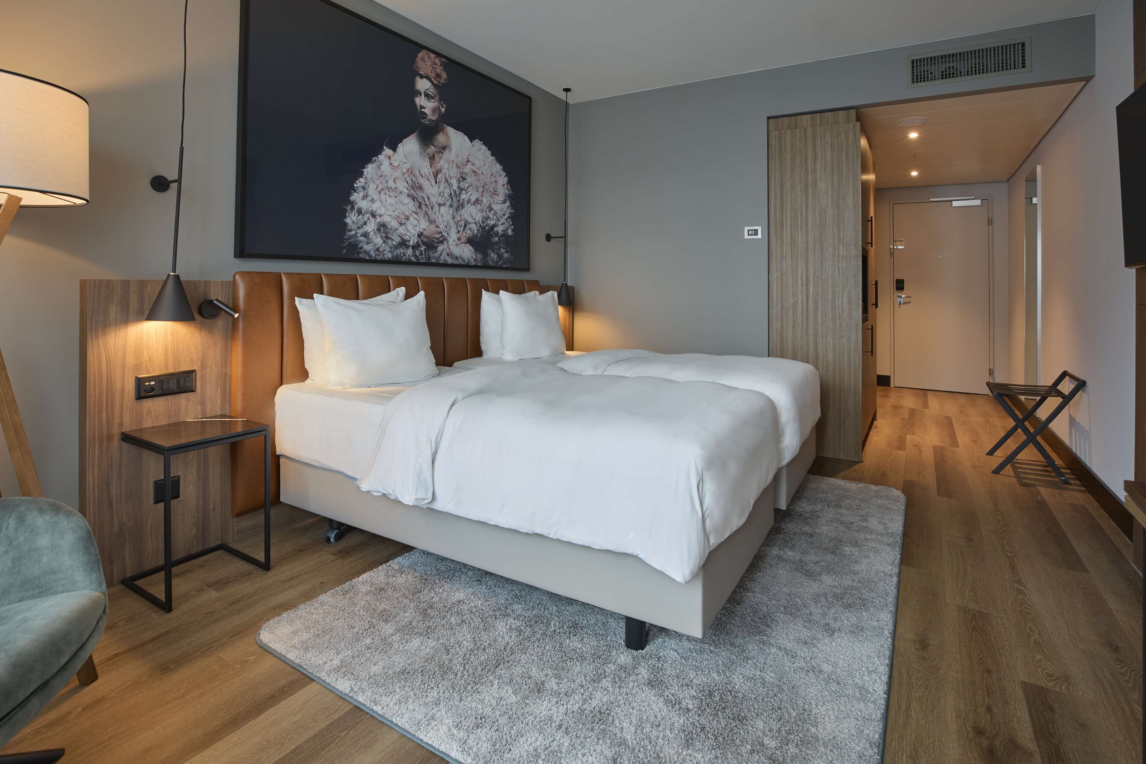 A modern hotel room with a large bed, a side table, a lamp, and a painting on the wall.