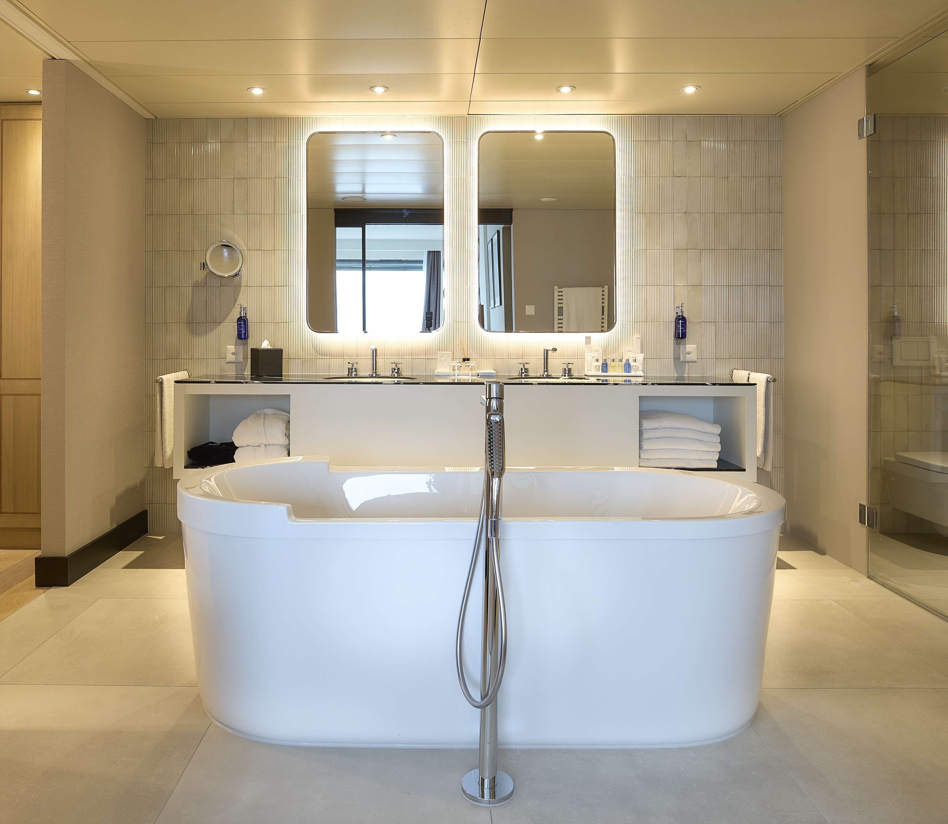 Un baño moderno con una bañera independiente, un espejo grande y un tocador con lavabo y perchero para toallas.