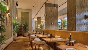 Un restaurante con mesas y sillas de madera, plantas en macetas y un ventanal grande.