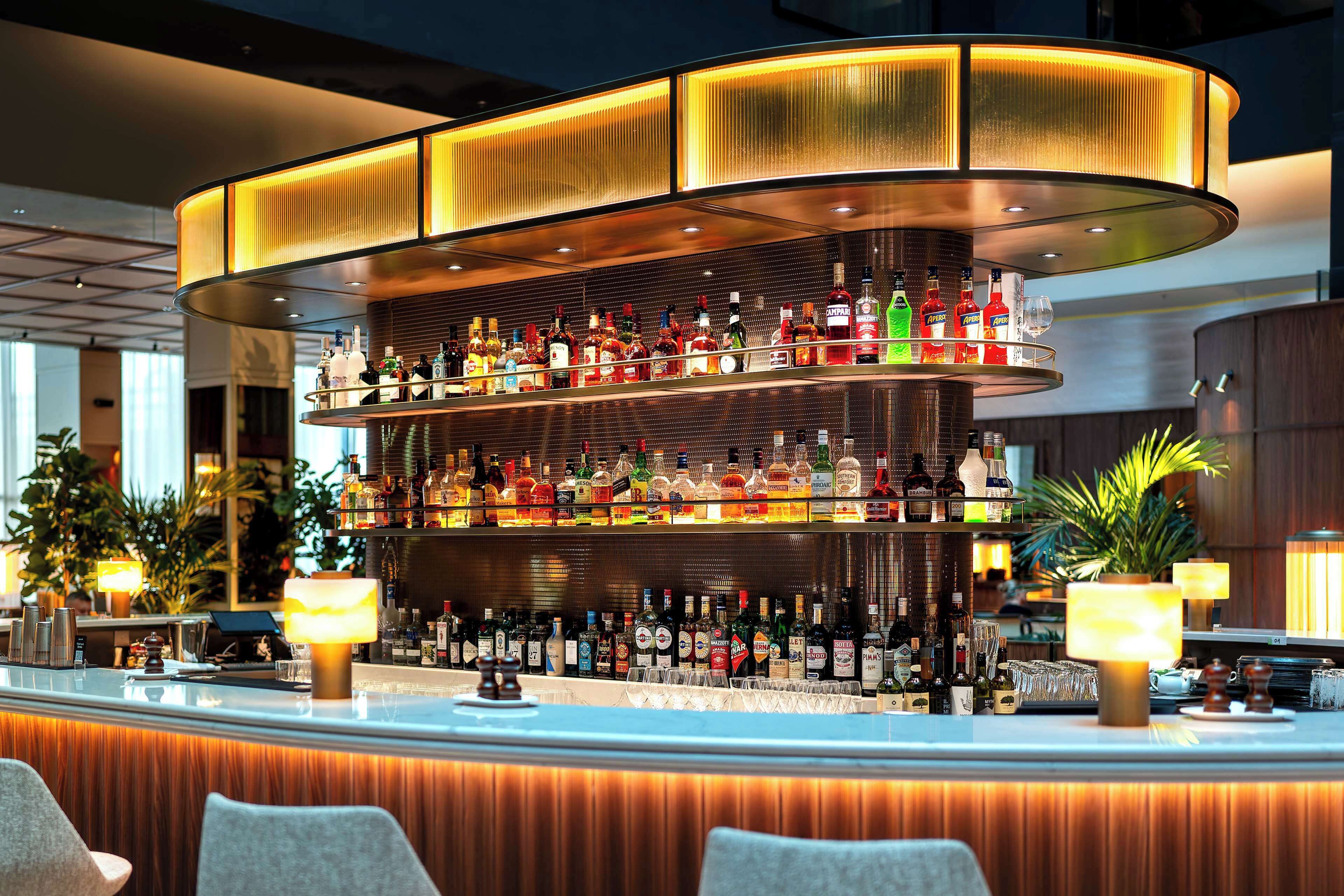 Un bar con estantes llenos de botellas de licor, una barra curva y dos lámparas.