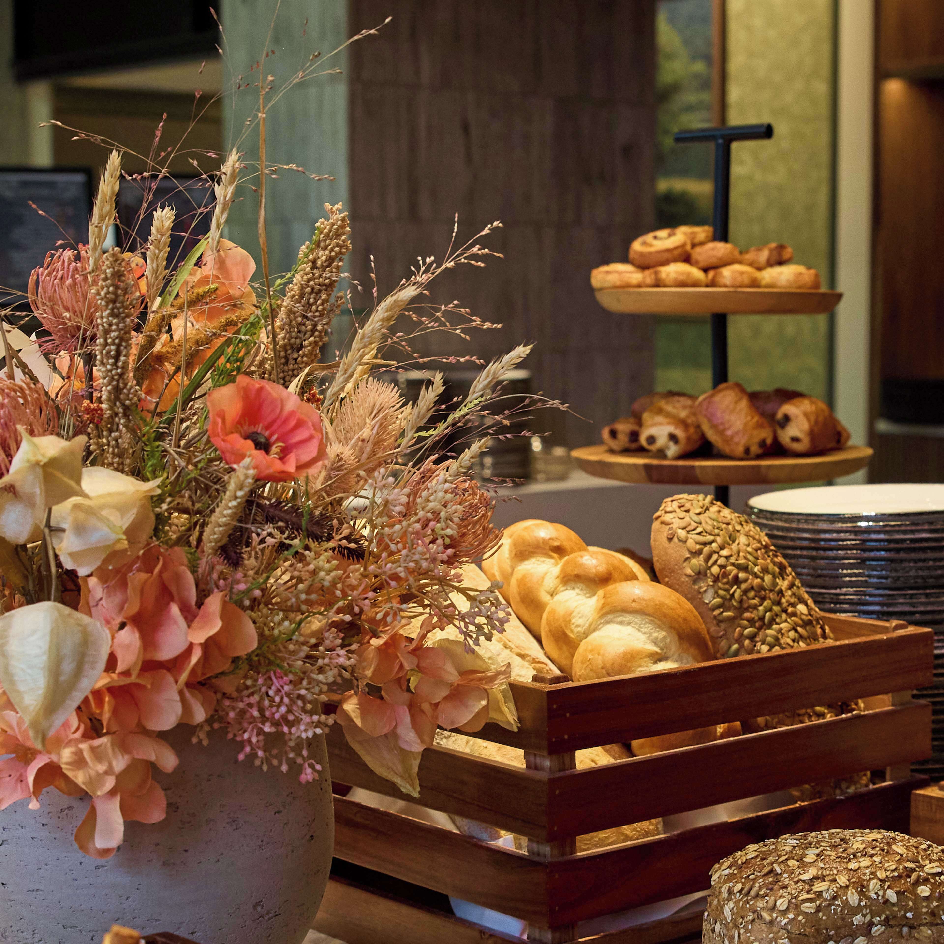 A bakery display with bread and pastries, a wooden crate, and a floral arrangement.