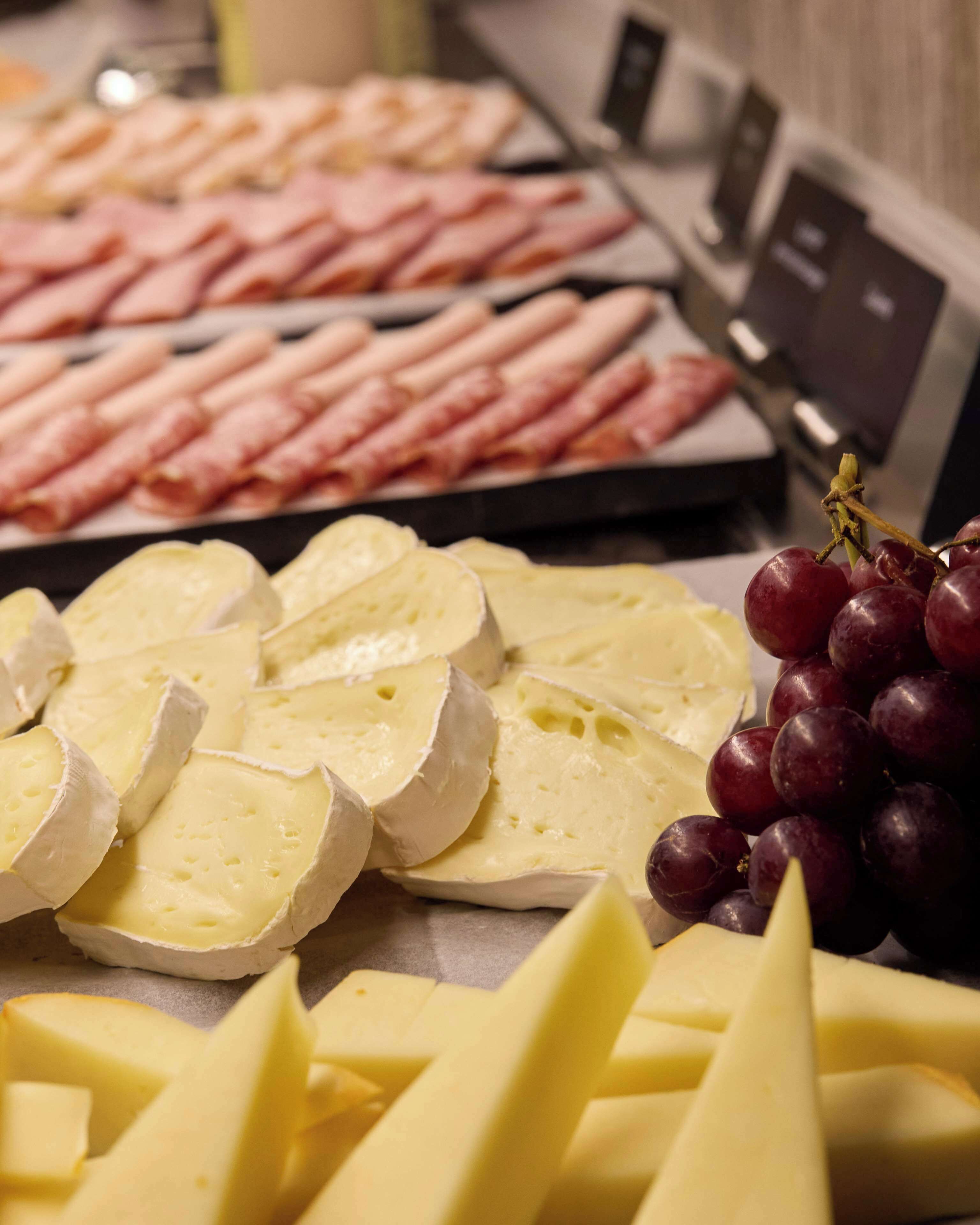 Un plateau de fromages et de jambon, comprenant des tranches de fromage, des raisins et des tranches de jambon.