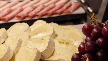Un plateau de fromages et de jambon, comprenant des tranches de fromage, des raisins et des tranches de jambon.