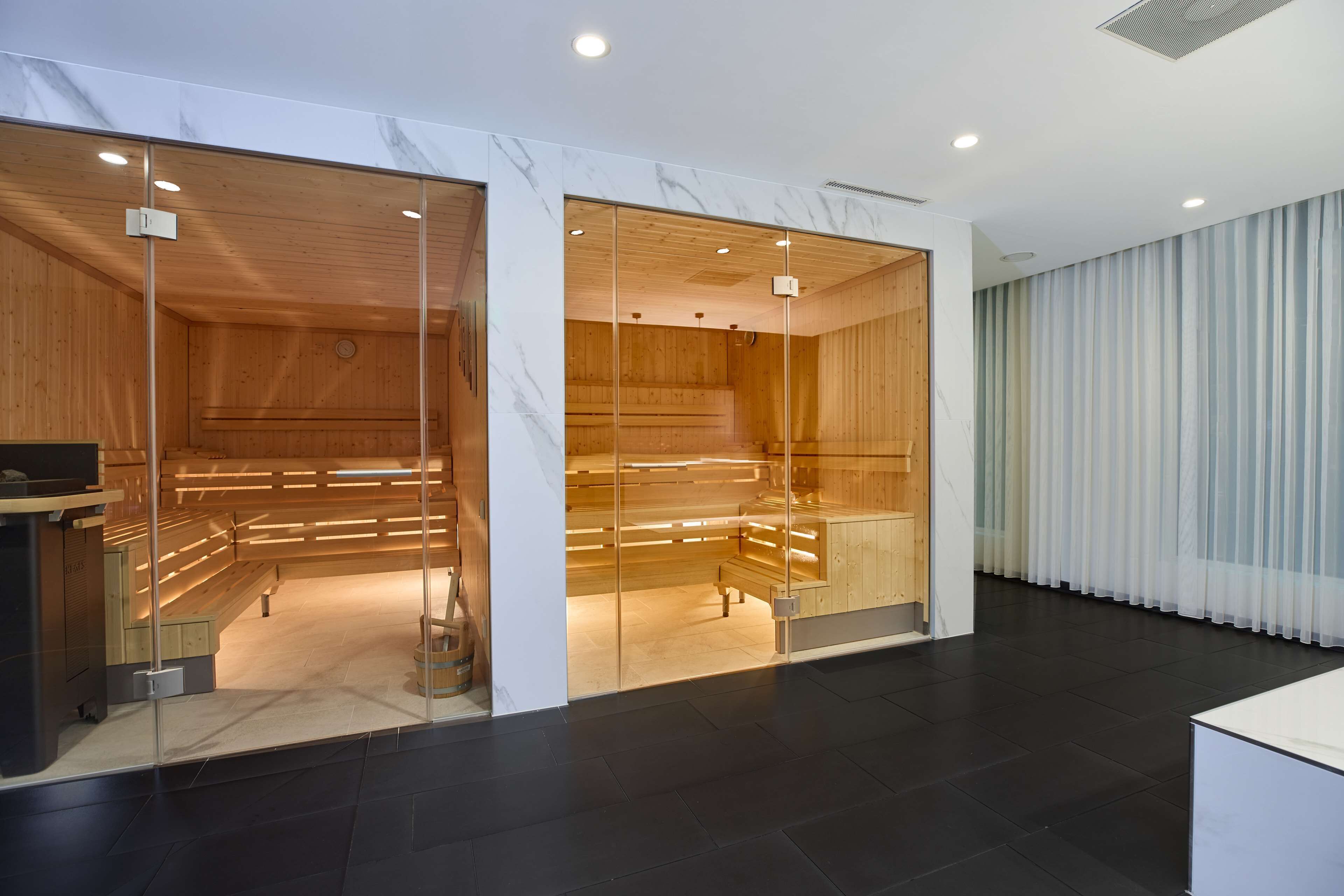 Ein moderner Spa-Bereich mit Holzbänken und Glaswänden, einem Empfangstresen und einem großen Fenster mit Vorhängen.