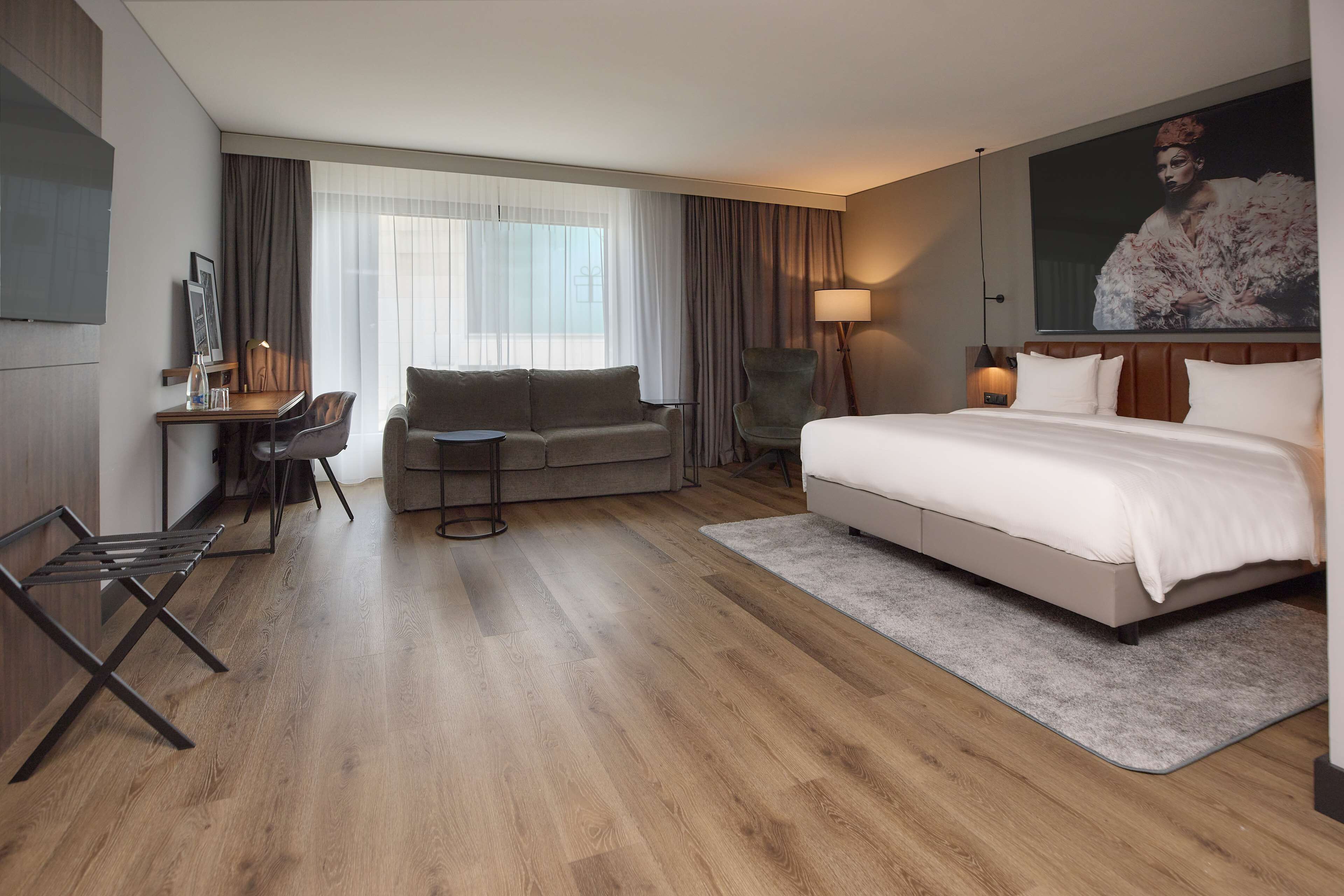 A modern hotel room with a large bed, a sofa, a desk, and a chair.