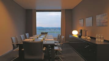 Une salle de conférence avec une longue table, des chaises, une vue sur l’aéroport et un comptoir d’accueil agrémenté d’une lampe et de bouteilles d’eau.