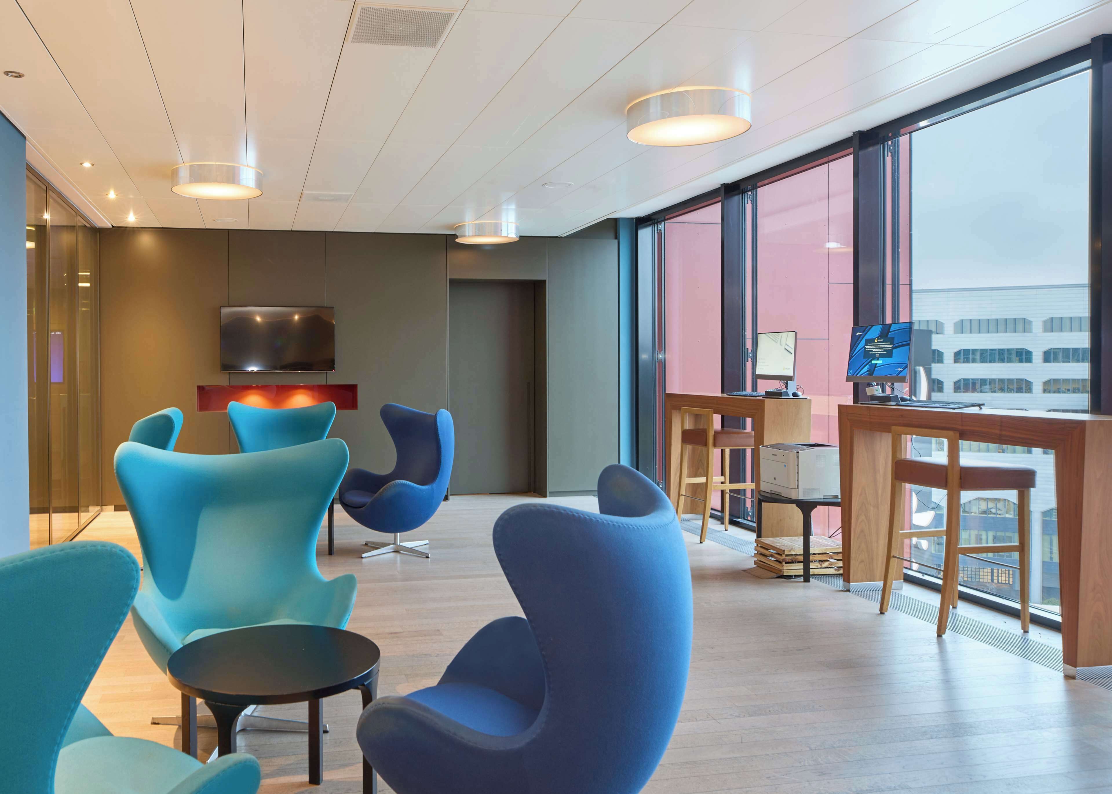 A modern lounge area with blue chairs, a TV, and a desk with a computer.