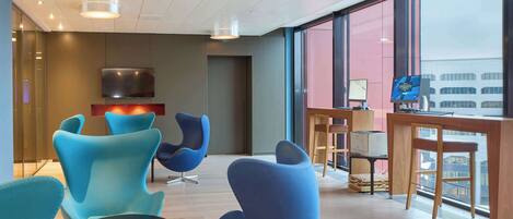 A modern lounge area with blue chairs, a TV, and a desk with a computer.