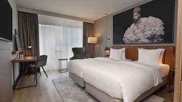 Een hotelkamer met een groot bed, een bureau met stoel, een klein tafeltje en een groot raam met gordijnen.