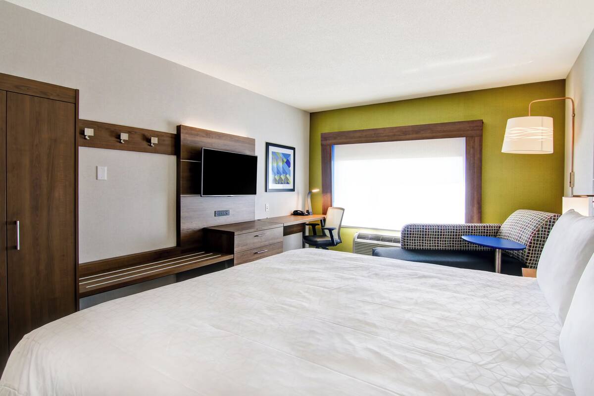 Une chambre d’hôtel avec un grand lit, un bureau doté d’un téléviseur à écran plat, une chaise et une fenêtre avec des stores.