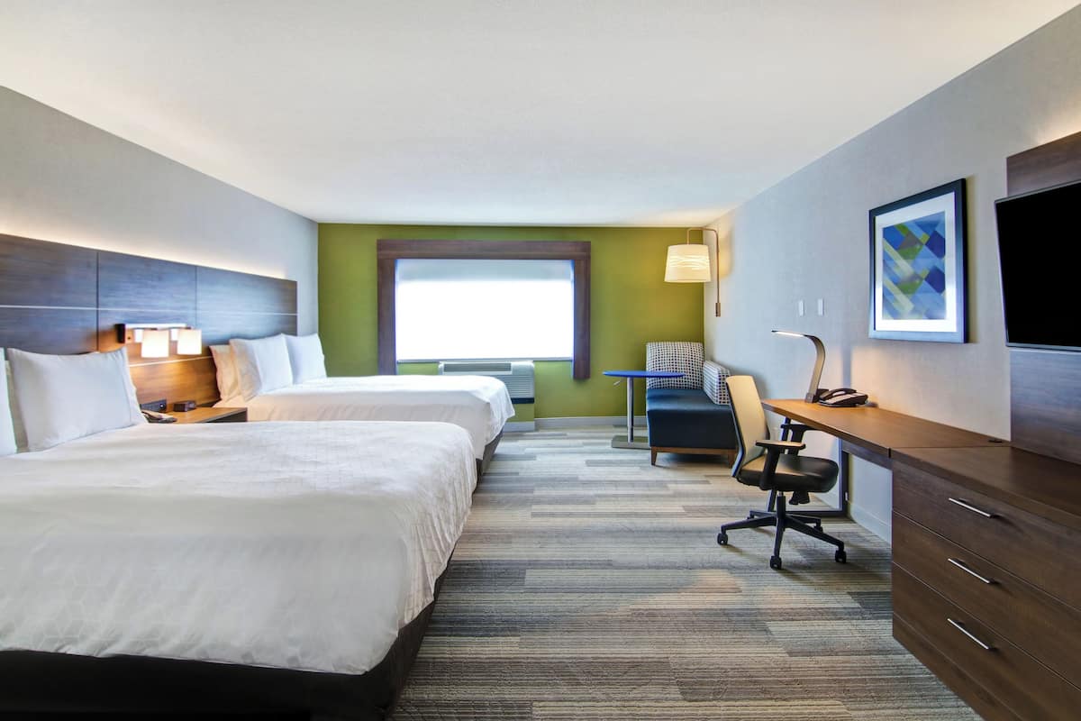 Une chambre d’hôtel avec deux lits, un bureau, une chaise, une télévision et une fenêtre.