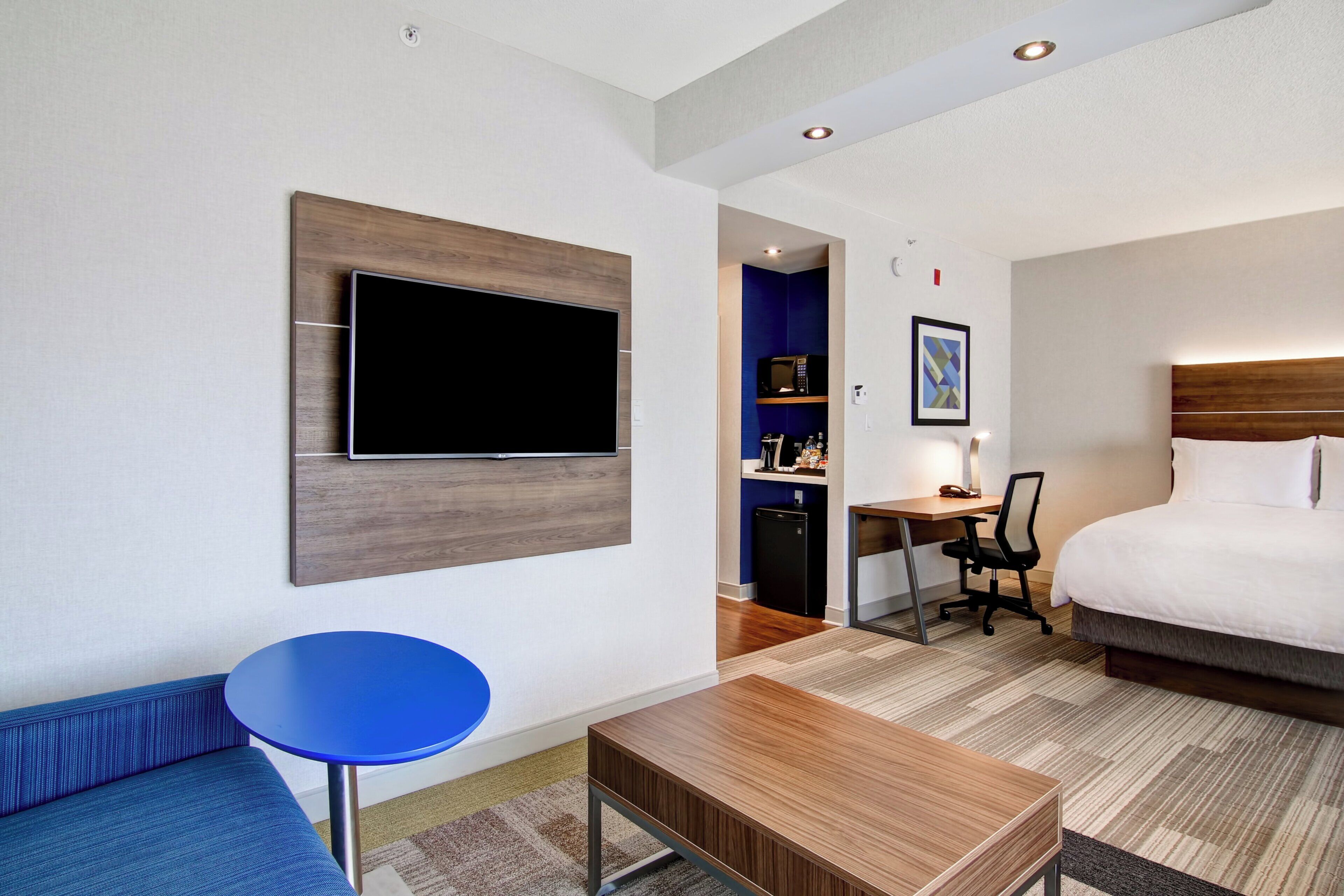 Une chambre d’hôtel avec un lit, un bureau, une chaise, un téléviseur fixé au mur et une petite table bleue.