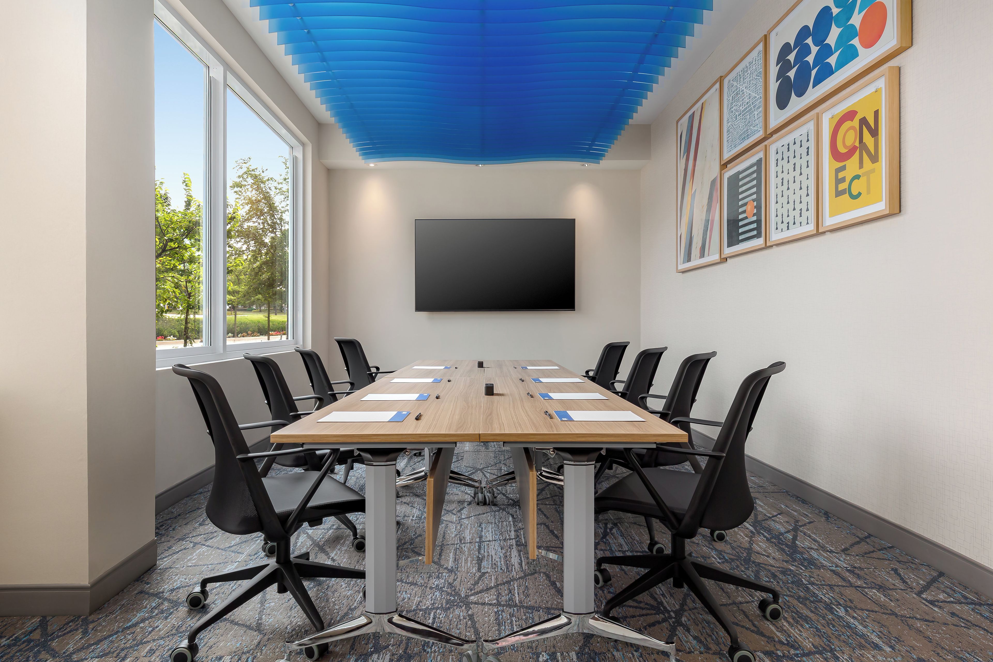 Una sala conferenze con un lungo tavolo, sedie nere, un televisore a schermo piatto e opere d'arte incorniciate al muro.
