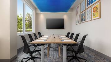 A conference room with a long table, black chairs, a flat-screen TV, and framed artwork on the wall.
