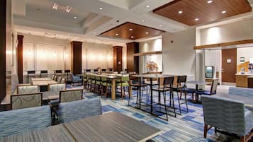 Comedor de hotel con varias mesas y sillas, zona de cocina y mostrador con menú.