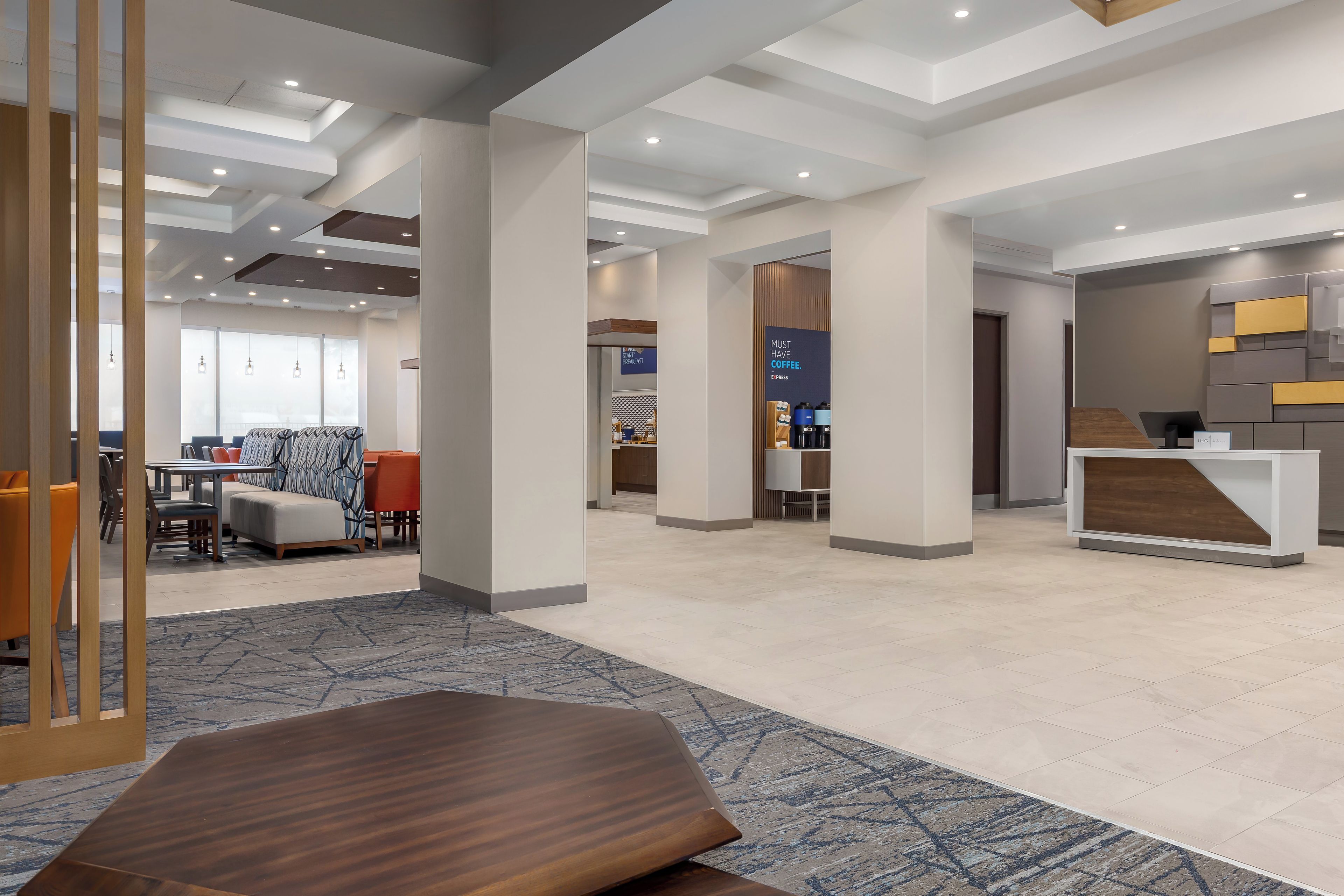 A modern hotel lobby with a reception desk, seating area, and a sign indicating a breakfast area.
