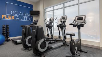 A gym with cardio equipment, a wall with motivational text, and a large window.