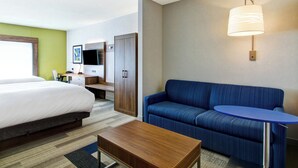 A hotel room with a bed, a desk, a blue sofa, a small table, and a wall-mounted lamp. - Holiday Inn Express Hotel & Suites Toronto - Markham by IHG (Richmond Hill)