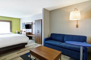 A hotel room with a bed, a desk, a blue sofa, a small table, and a wall-mounted lamp. - Holiday Inn Express Hotel & Suites Toronto - Markham by IHG (Richmond Hill)