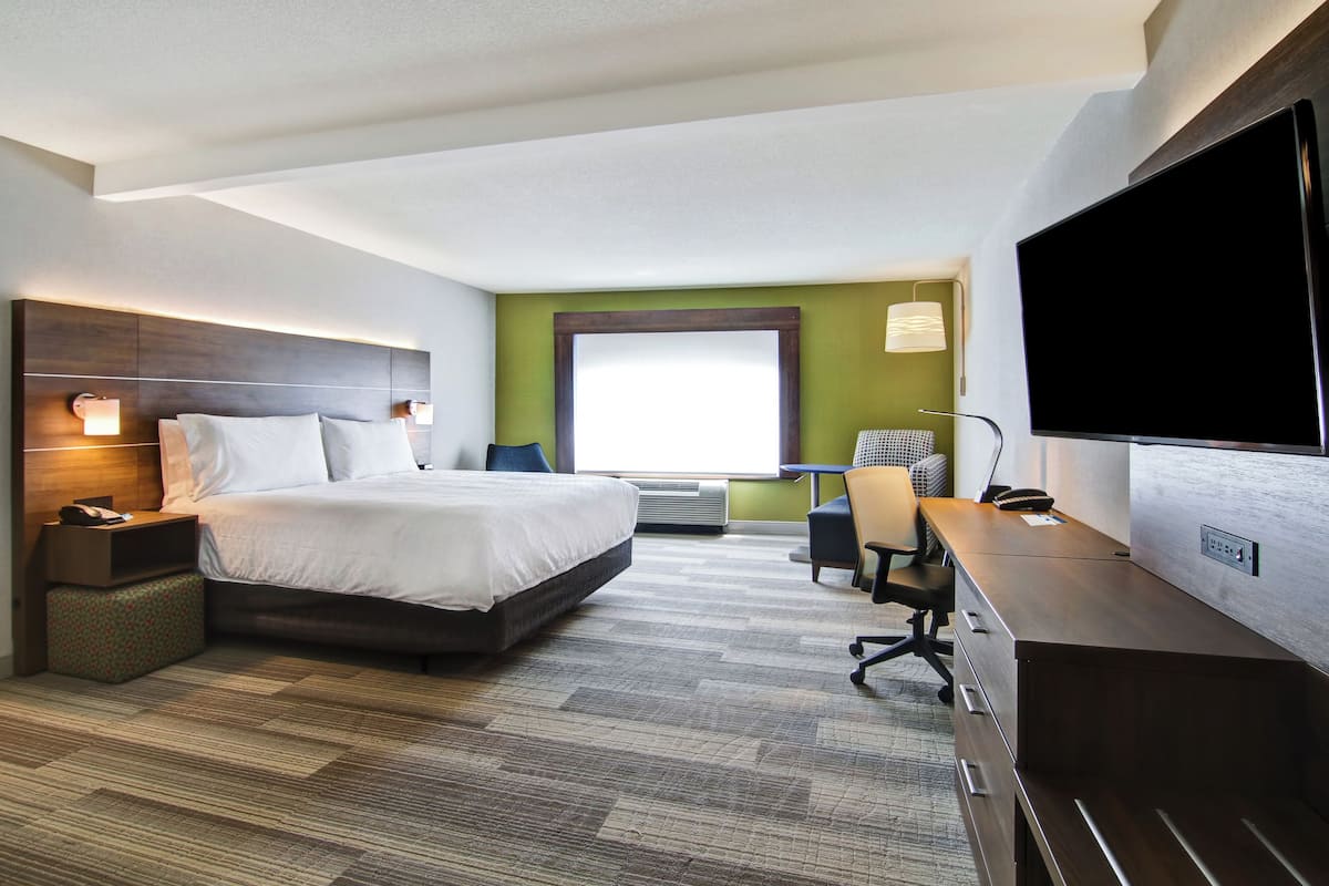 Une chambre d’hôtel équipée d’un lit, d’un bureau, d’une chaise, d’une télévision et d’une fenêtre donnant sur un paysage agréable.