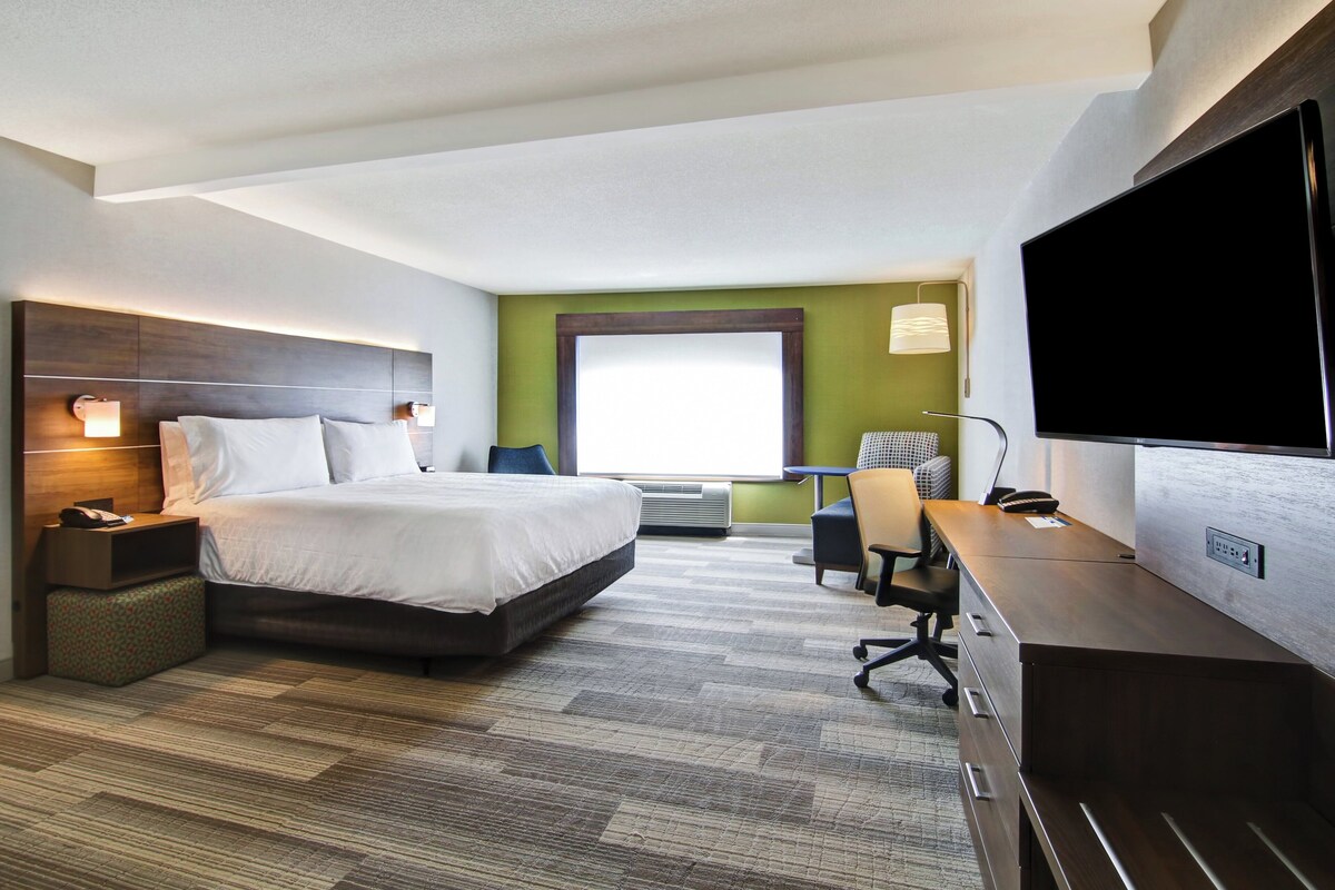 A hotel room with a bed, desk, chair, TV, and a window.