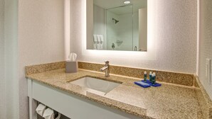 A bathroom with a granite countertop, a sink, a mirror, and a shower visible in the reflection. - Holiday Inn Express Hotel & Suites Toronto - Markham by IHG (Richmond Hill)