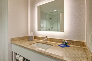 A bathroom with a granite countertop, a sink, a mirror, and a shower visible in the reflection. - Holiday Inn Express Hotel & Suites Toronto - Markham by IHG (Richmond Hill)