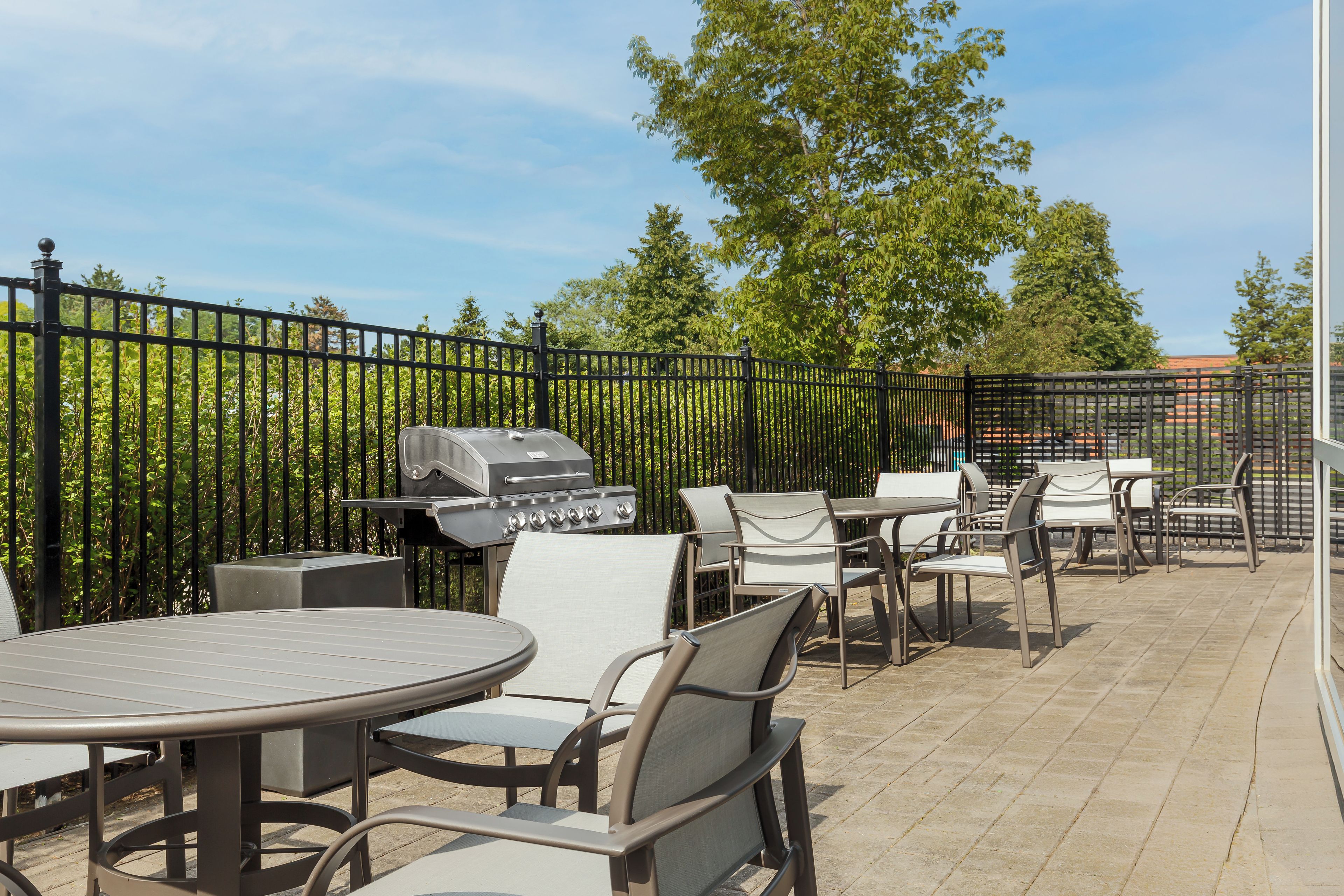 An outdoor patio area with tables and chairs, a barbecue grill, and a metal fence.