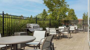 An outdoor patio area with tables and chairs, a barbecue grill, and a metal fence.