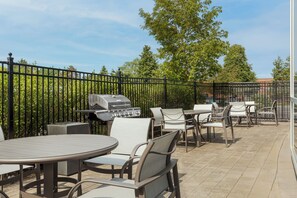 An outdoor patio area with tables and chairs, a barbecue grill, and a metal fence.