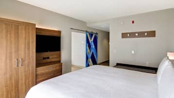 A hotel room with a large bed, wooden wardrobe, a flat-screen TV, a shower curtain, and a wall-mounted light switch.