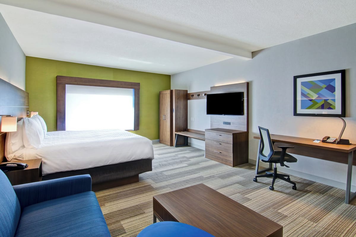 Une chambre d’hôtel moderne avec un grand lit, un bureau, une chaise, une télévision et un tableau au mur.