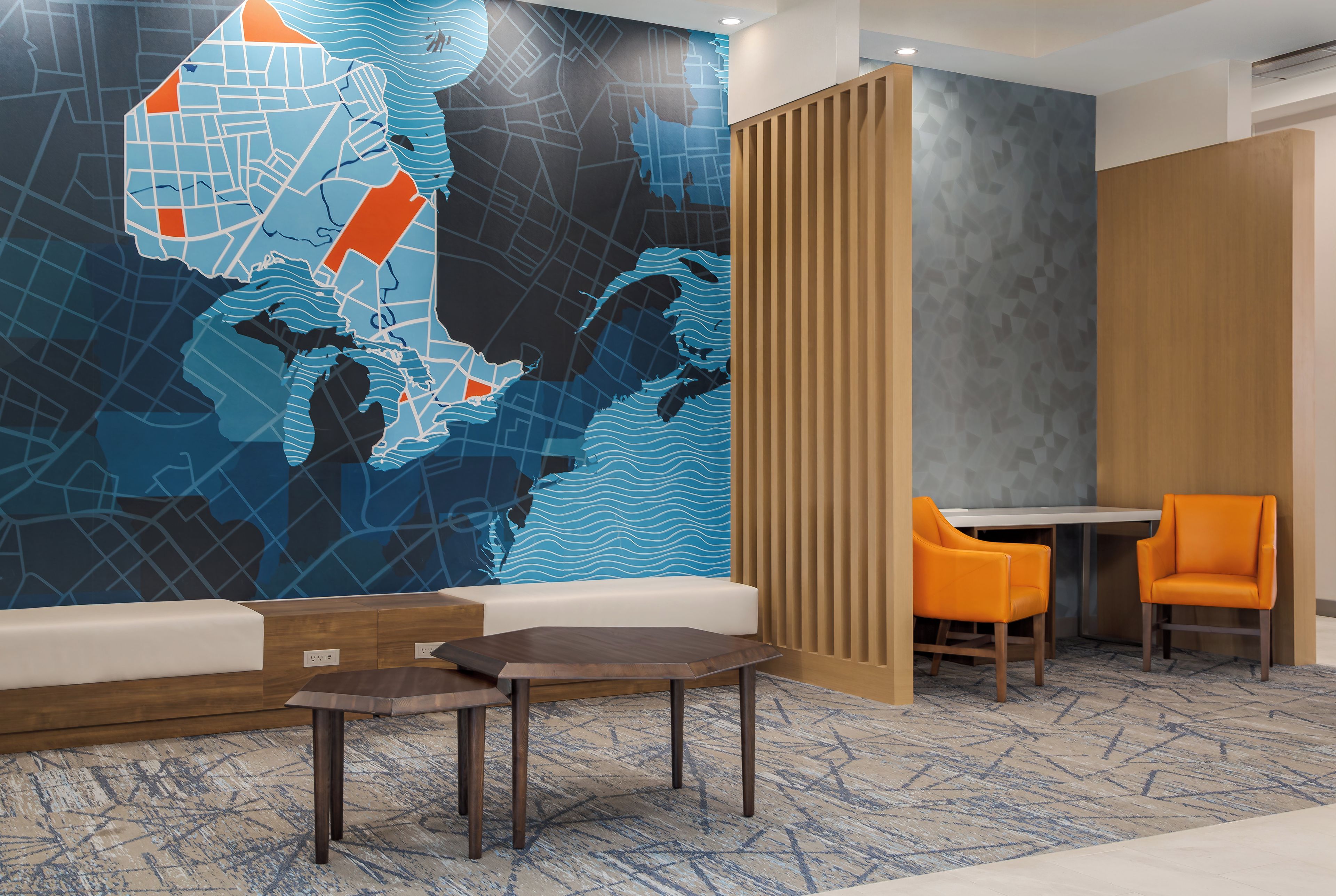Un vestíbulo de hotel con un mural grande en la pared, un mostrador de recepción y dos sillones naranja.