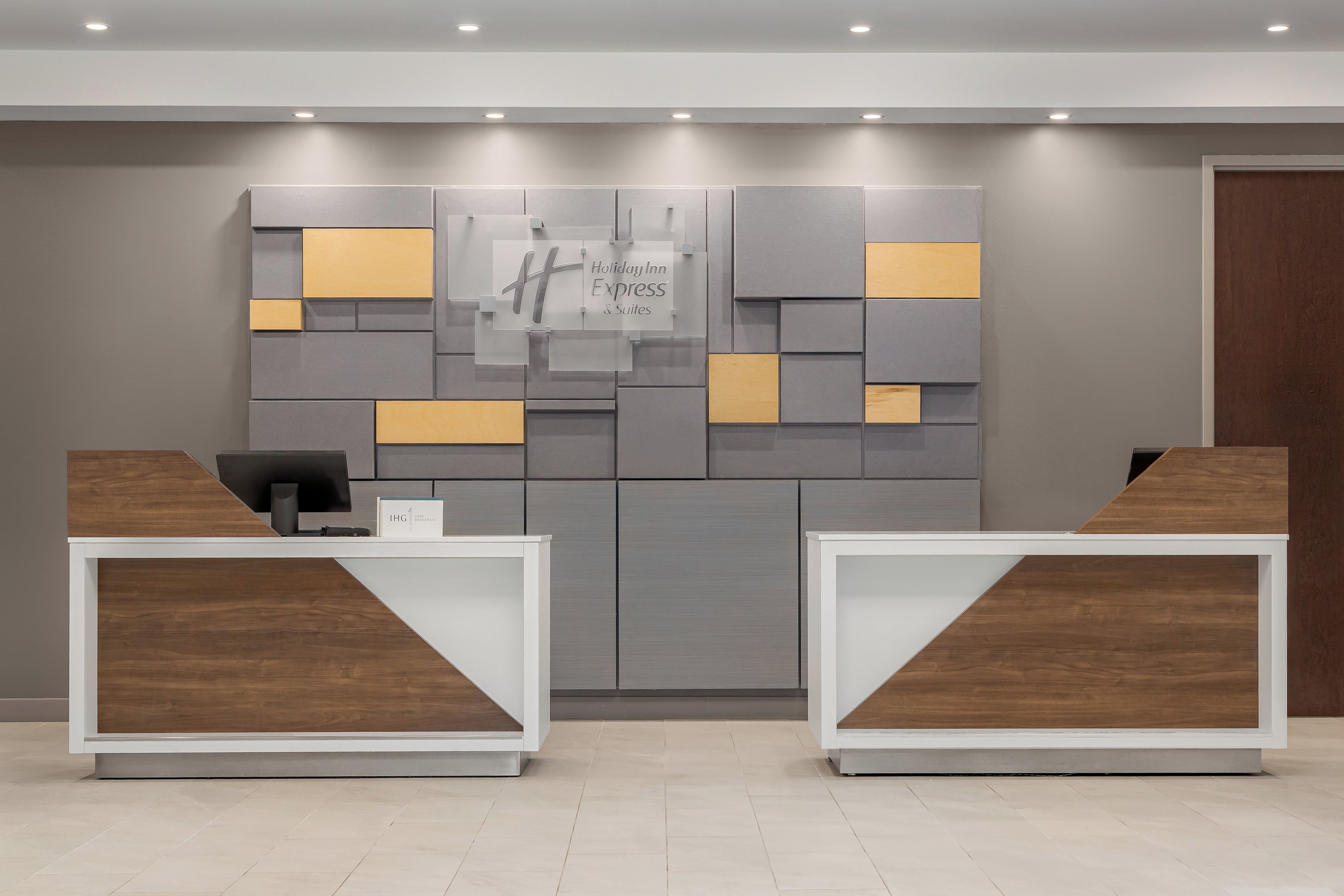 Zona de recepción con un cartel de Holiday Inn Express, dos mostradores de recepción y un diseño moderno de pared.