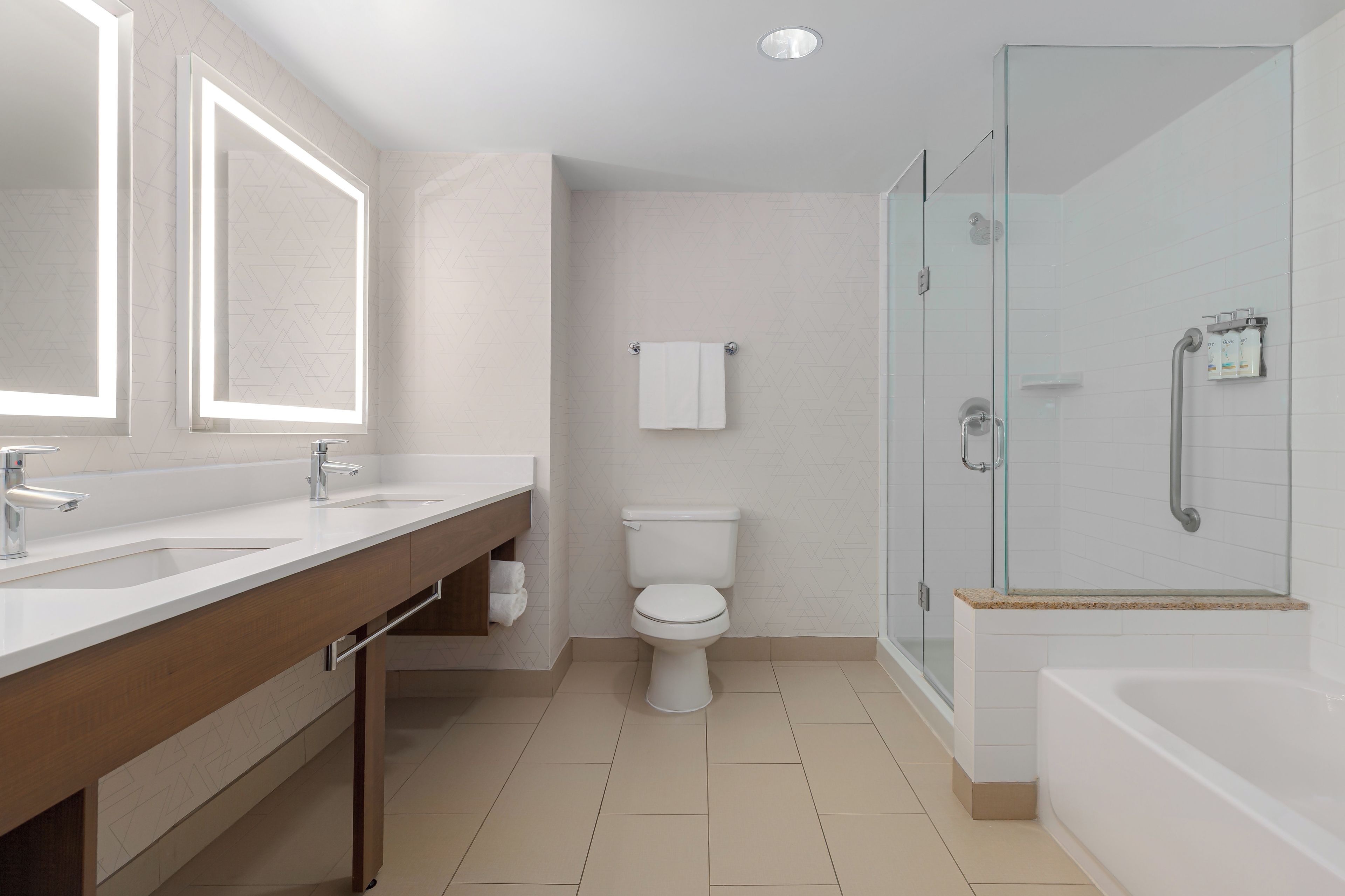 A modern bathroom with a double vanity, a toilet, a glass shower enclosure, and a bathtub.