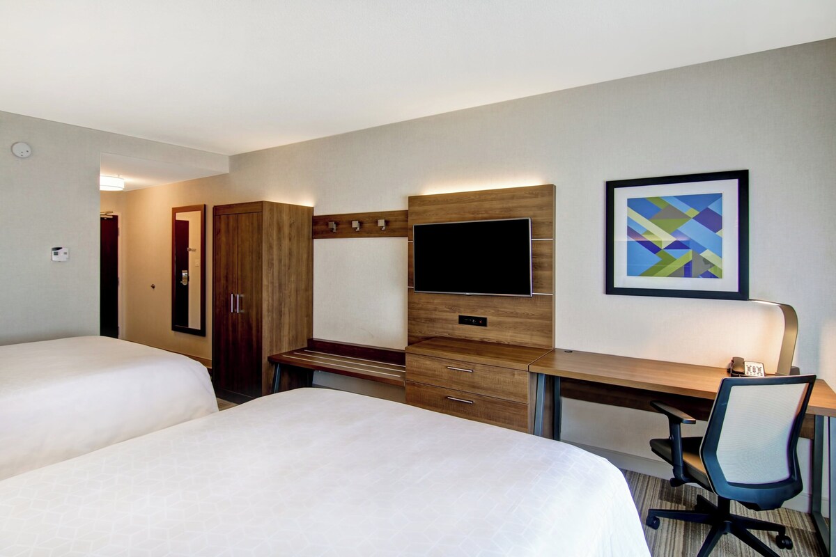 A hotel room with two beds, a desk, a TV, and a framed abstract painting.