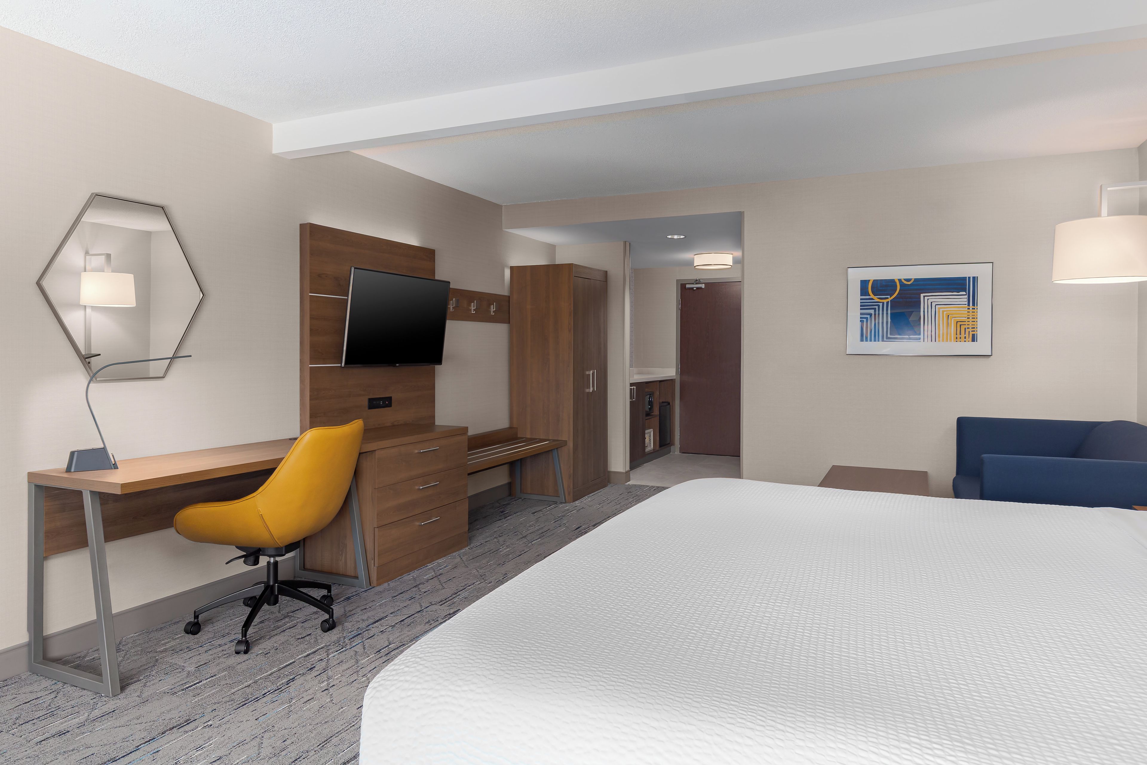 Une chambre d’hôtel avec un lit, un bureau et une chaise, une télévision, une porte et un tableau au mur.