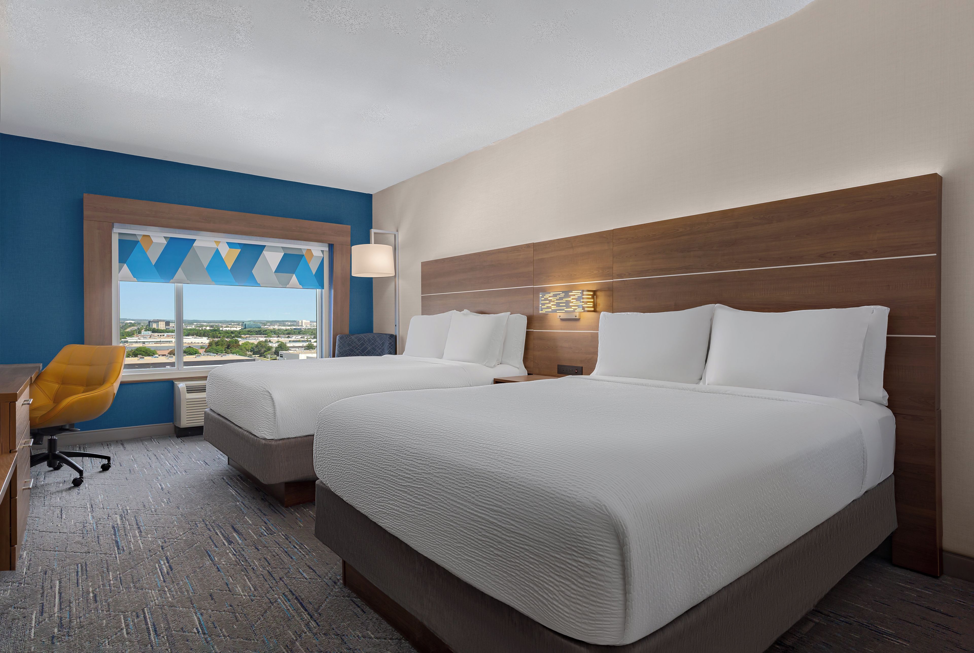 A hotel room with two beds, a desk, a chair, and a window with a view.