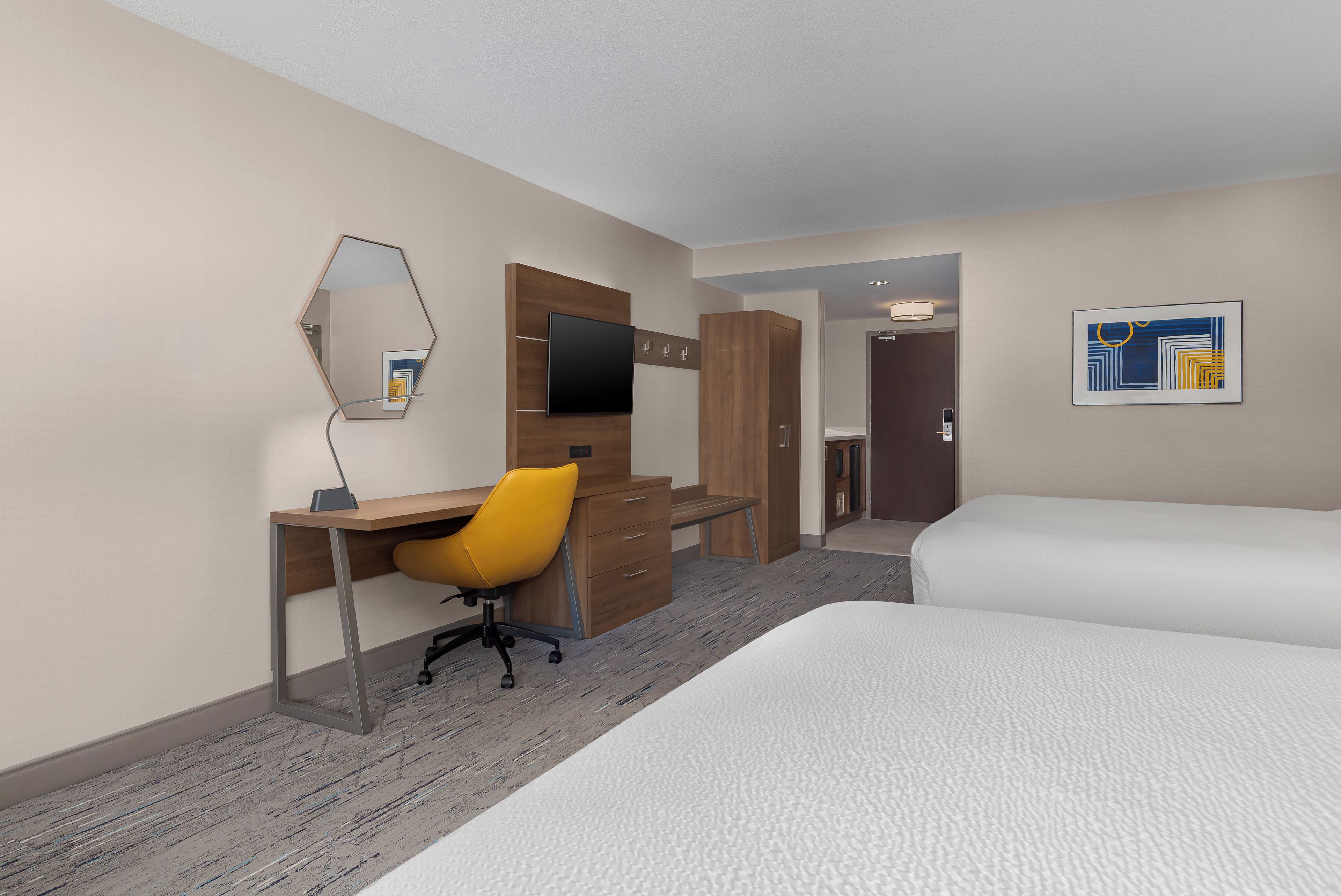 A hotel room with a desk, chair, bed, and a large mirror.