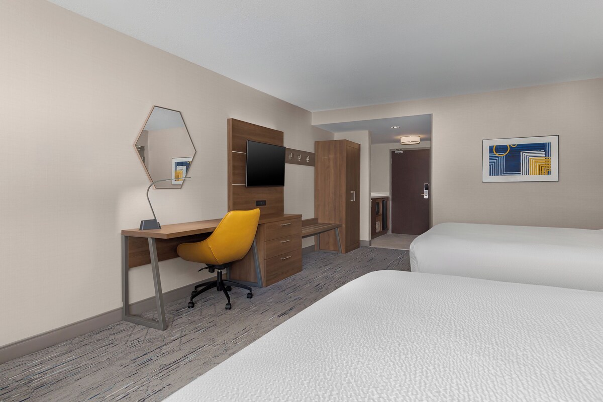 A hotel room with a desk, chair, bed, and a large mirror.